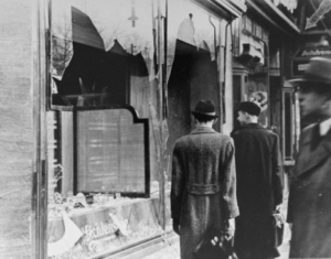 Two men looking at two broken glass windows of a store front